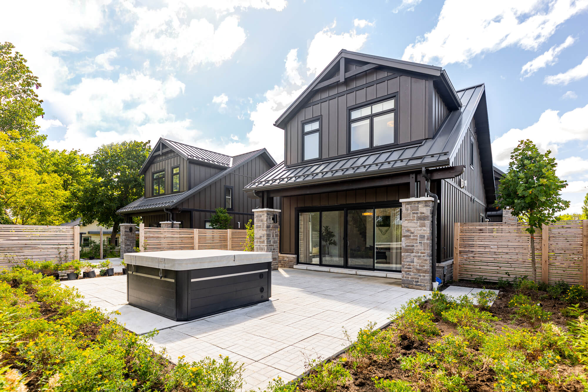 Exterior of modern VRBO rental in Ontario — dark board and batten siding, metal roof, hot tub on paver patio and sliding glass doors to interior